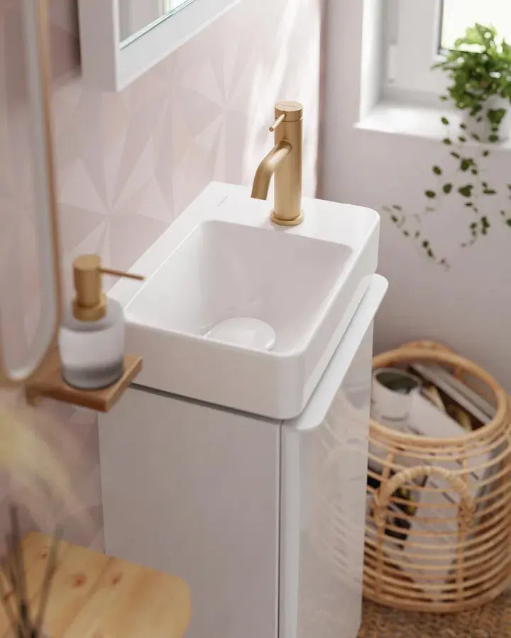 Modern white bathroom sink with gold Hansgrohe faucet, soap dispenser, geometric wall tiles, and woven basket nearby.