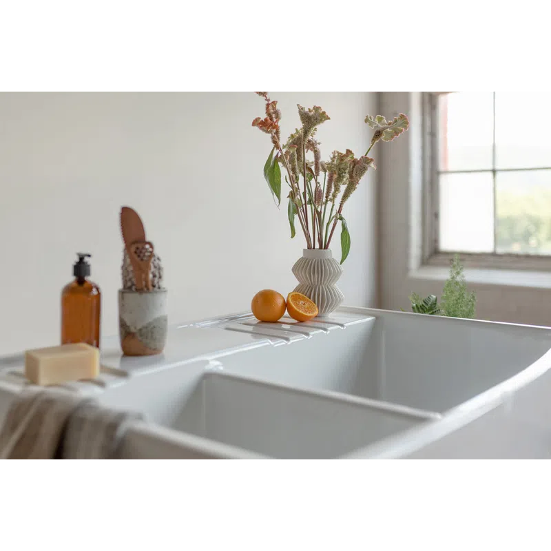 White farmhouse sink with dried flowers in a vase, sliced oranges, soap, and a towel in soft natural light.