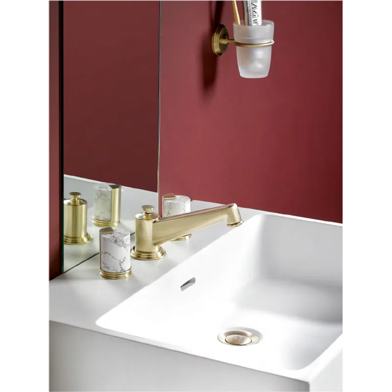 Modern bathroom sink with gold faucet, marble soap dispenser, and deep red wall with mirror reflection.