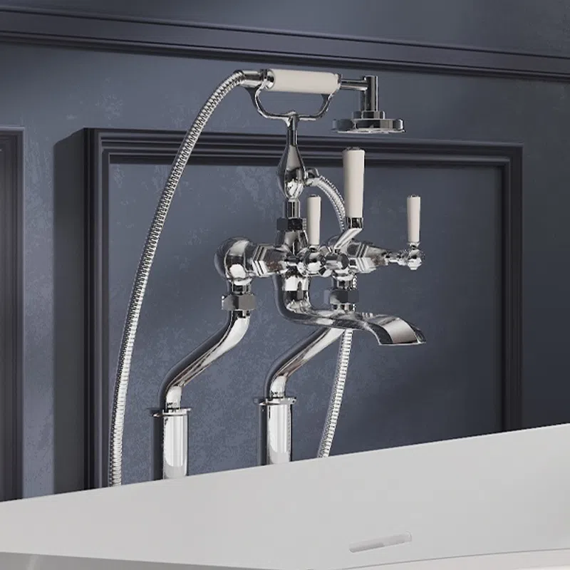 Polished chrome wall-mounted bathtub faucet with handheld shower and white ceramic handles on dark blue wall.